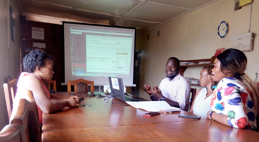 Two women and one man sit around a table with laptop, smiling